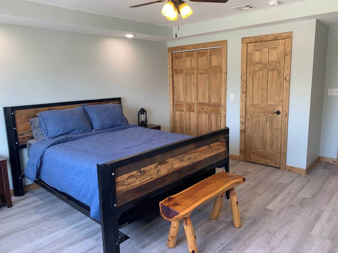 A bedroom with a wooden bed frame, a bench, and two wooden doors.