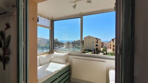 Uma varanda com um banco acolchoado branco, vista para edifícios e céu claro.
