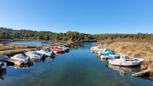 Um rio calmo com barcos atracados nas margens, rodeado por áreas gramadas e árvores.
