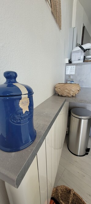 A kitchen with a blue container, a stainless steel trash bin, and a woven basket on the counter. - Like a Fish in Water – Apartment with an Ocean View (Saint pierre la mer)