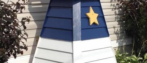 Una struttura decorativa a forma di faro, con una combinazione di colori rosso, bianco e blu, e una stella gialla sul lato.