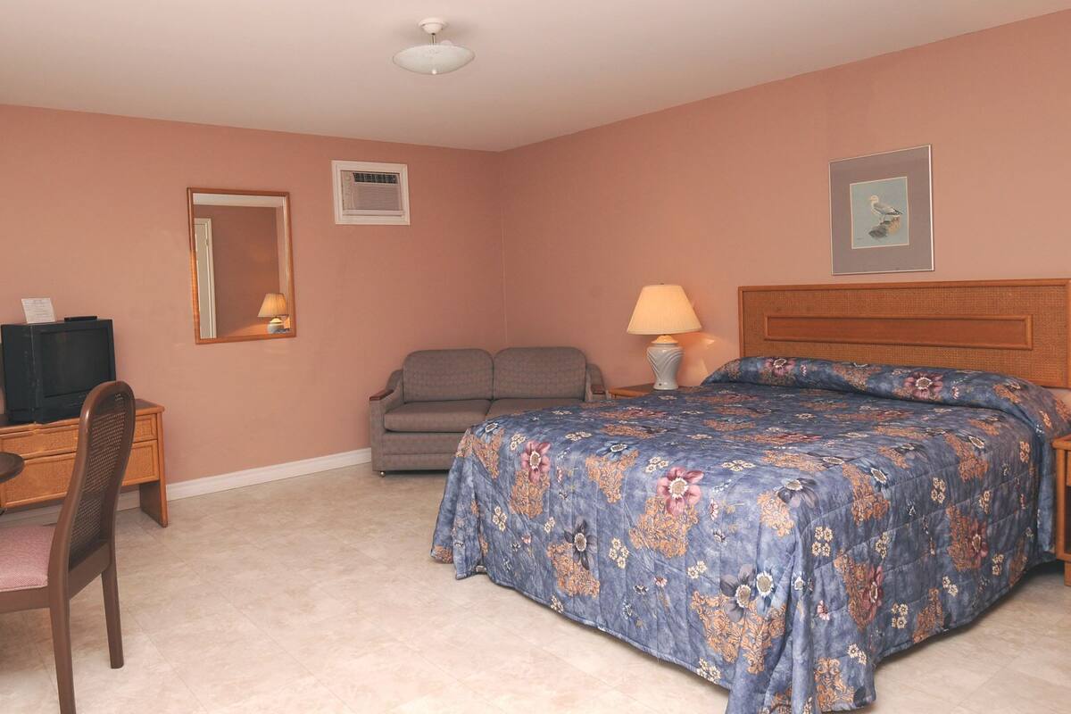 Ein Hotelzimmer mit Bett, Schreibtisch mit Stuhl, Fernseher, Sofa und Lampe.