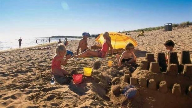 A sandy beach with people playing and building sand structures. - Gaudet Chalets & Motel (Shediac)