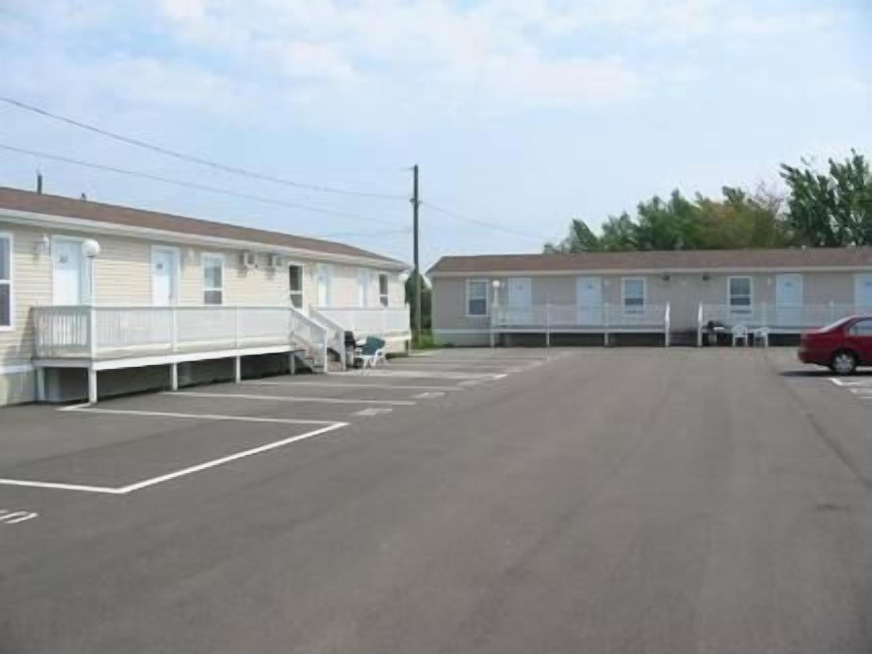 Un motel con estacionamiento, un coche rojo aparcado y un pequeño espacio de esparcimiento al aire libre.