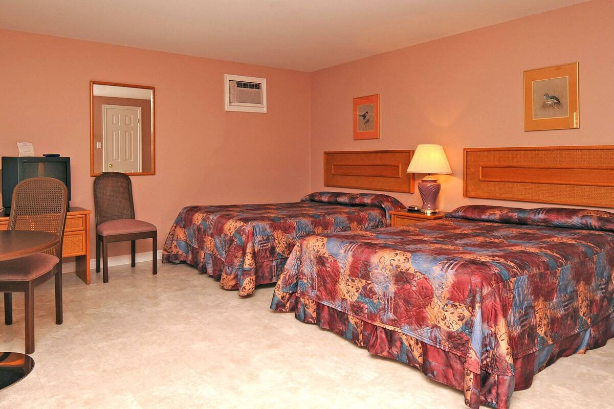 Ein Hotelzimmer mit zwei Betten, einem Schreibtisch mit Stuhl, einem Fernseher und einer Lampe.