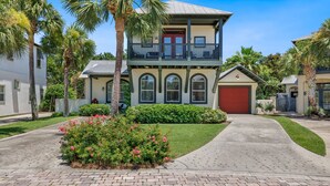 A two-story house with a balcony, a garage, and a well-maintained garden with pink flowers.