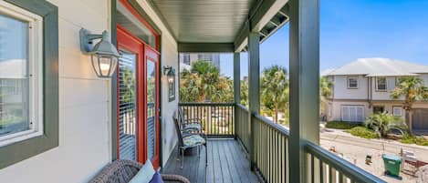 A covered porch with a sofa and chairs, a red door, and a view of a residential street.