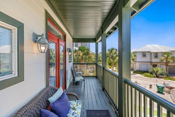 A covered porch with a sofa and chairs, a red door, and a view of a residential street.