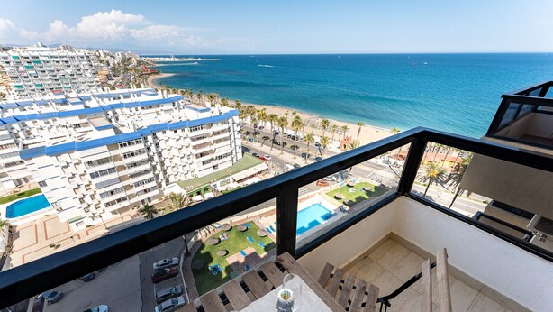 A balcony with a view of a beach, a pool, and a building complex. - MalagaSuite Aloha Playa (Benalmádena)