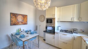 Une cuisine moderne avec des armoires blanches, un four en acier inoxydable, un four à micro-ondes et une cuisinière à gaz. On y trouve une table à manger avec des chaises bleues et un lustre au-dessus.