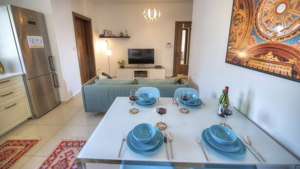 Un salon moderne avec une table à manger pour quatre personnes, un téléviseur à écran plat, un lustre et une grande fresque décorative au plafond.