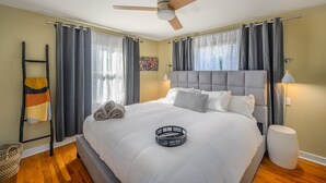 Un lit bien fait, avec une tête de lit, un ventilateur de plafond et une table de chevet avec une lampe.