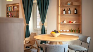 Un'area pranzo con un tavolo rotondo in legno, due sedie, una ciotola di frutta, una libreria e uno scaffale con bottiglie.