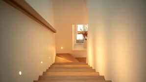 Una moderna scala con gradini in legno e illuminazione a incasso, che conduce a un pianerottolo con vista su una finestra e un vaso con fiori.