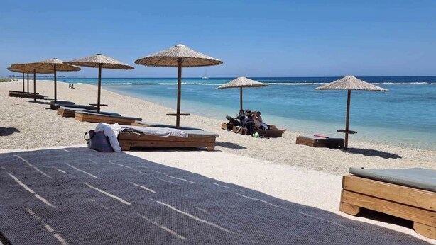 Une plage avec des chaises longues en bois et des parasols en chaume.