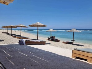 A beach with wooden lounge chairs and thatched umbrellas. - Villa Kallisti - private villa with hot tub, large garden, close to the beach (Agia Varvara-Peratia)