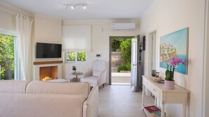 Un salon bien éclairé, avec un canapé, un téléviseur, une cheminée et un tableau accroché au mur.