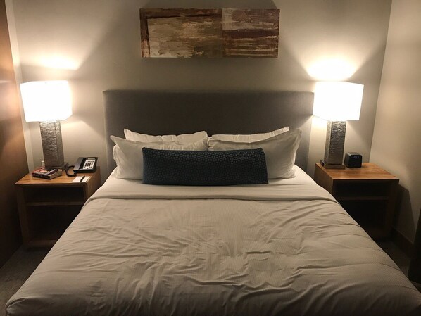 A neatly made bed with white linens, two bedside lamps, a phone, and a small table with a book and a lamp on each side.