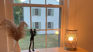 Un escritorio de madera con un jarrón blanco y plumas de pampa, una pequeña figurita negra y una lámpara encendida con motivos geométricos.