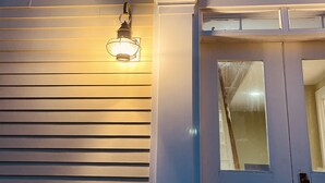 Fachada de una casa con revestimiento horizontal, una puerta principal y una lámpara exterior iluminada.