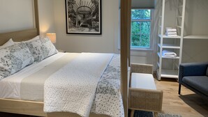 Un dormitorio con cama, mesita de noche, lámpara, cuadro enmarco, ventana, armario y una silla.