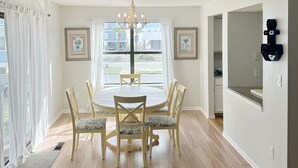 A dining room with a round table, six chairs, a chandelier, and framed artwork on the walls. - Pet Friendly 3 BR Condo across from beach! (Gulf Shores)