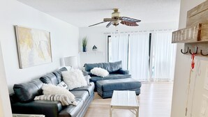 A modern living room with a dark leather sofa, a white coffee table, and a ceiling fan. - Pet Friendly 3 BR Condo across from beach! (Gulf Shores)