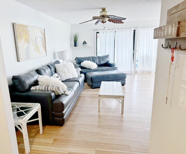 A modern living room with a dark leather sofa, a white coffee table, and a ceiling fan.