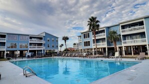 A swimming pool surrounded by multi-story buildings with balconies, palm trees, and lounge chairs. - Pet Friendly 3 BR Condo across from beach! (Gulf Shores)