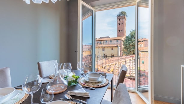 A dining area with a table set for four, overlooking a historic town with a prominent tower. - Casa Grey Contemporary Penthouse (Lucca)