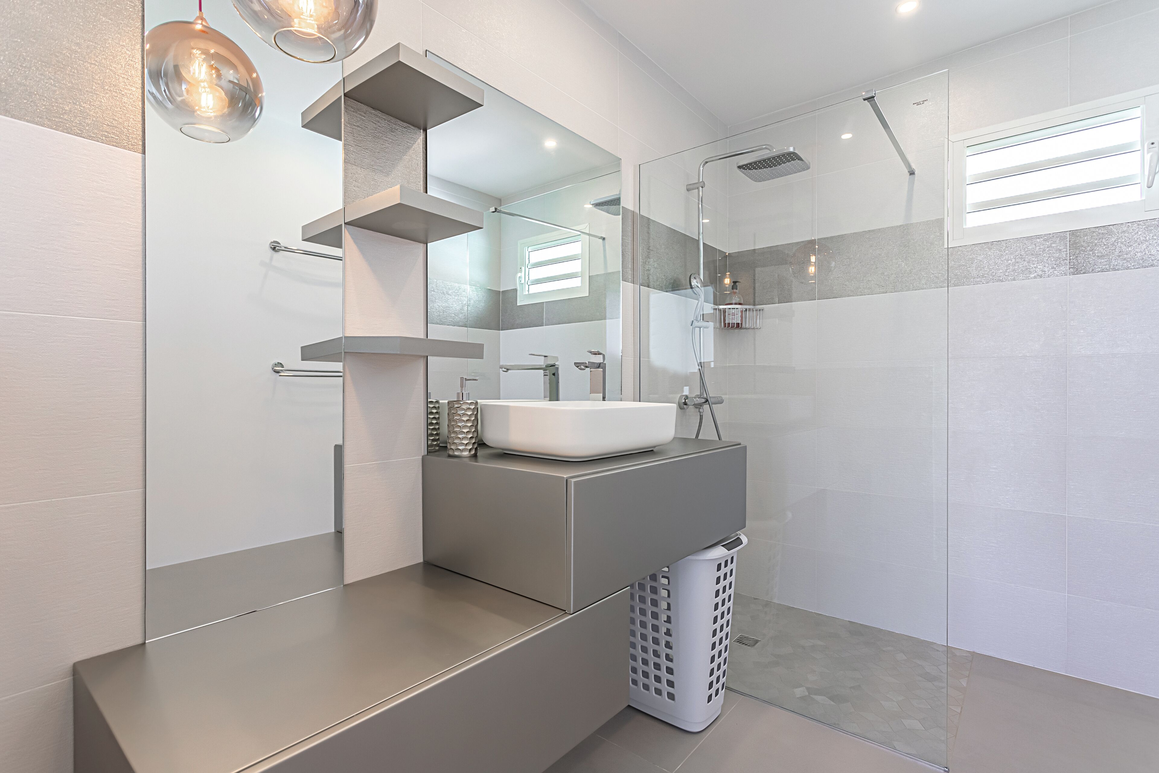 Un bagno moderno con un ampio specchio, un lavandino bianco e una cabina doccia in vetro.
