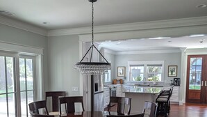 A spacious dining area with a large round table and chairs, a chandelier, and a view of the kitchen in the background. - Charming 4b/3b Newly Constructed Home on Dataw Island - Available 5/15 - 10/15 (Dataw Island)