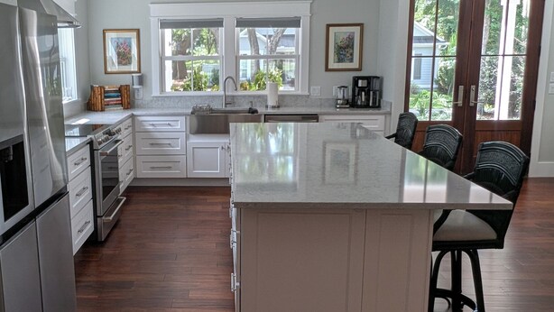 A modern kitchen with white cabinetry, a large island, and a dining area with bar stools. - Charming 4b/3b Newly Constructed Home on Dataw Island - Available 5/15 - 10/15 (Dataw Island)