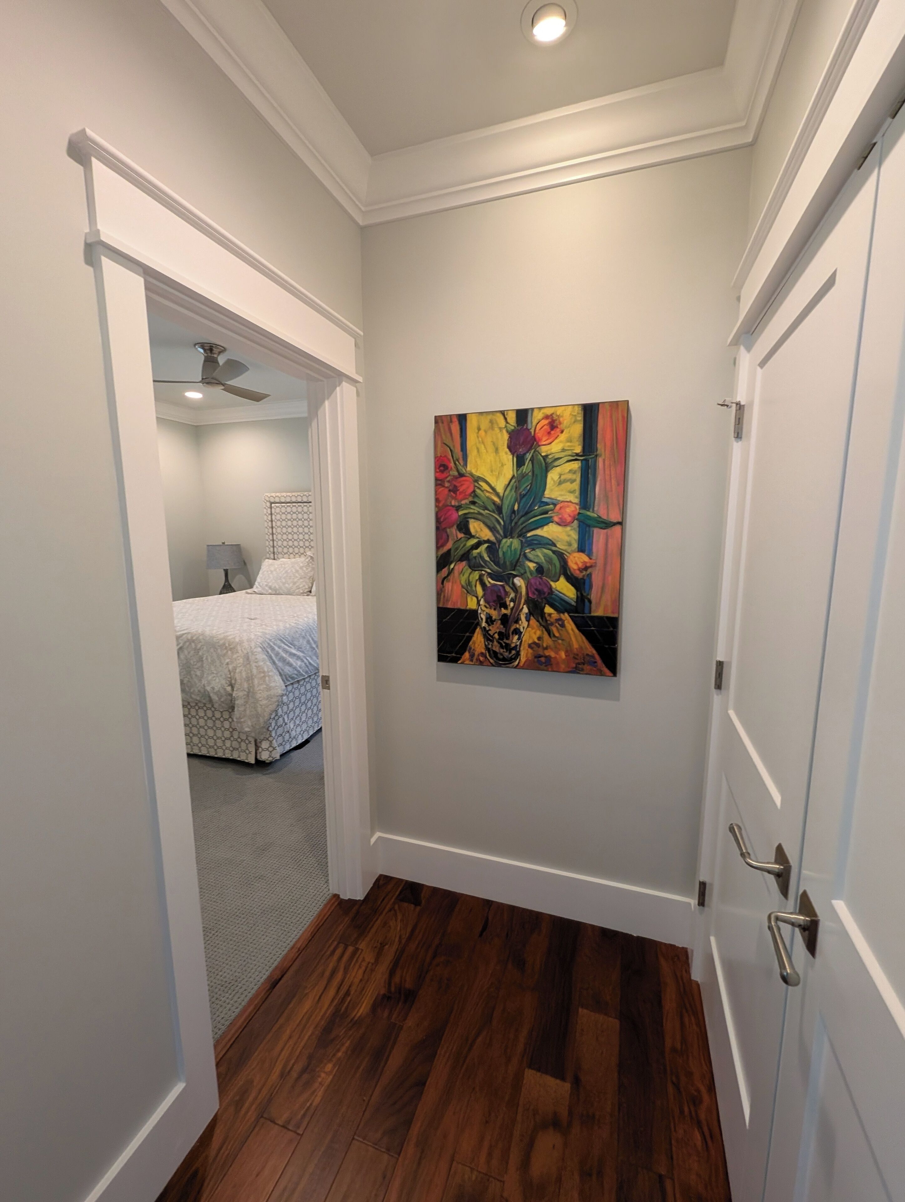 Un couloir avec un plancher en bois, un ventilateur de plafond et un tableau accroché au mur.
