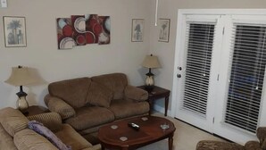 Un salon avec un ensemble de meubles marron, dont un canapé, une table basse et un ventilateur de plafond. On y trouve également des œuvres d’art murales et une porte avec des stores.