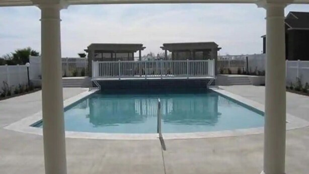 Une piscine couverte, entourée d’une clôture blanche, avec deux structures abritées en arrière-plan.