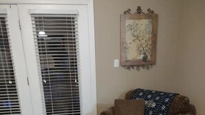 Un salon avec un canapé à motifs, un pouf, une table basse en bois et un tableau accroché au mur.