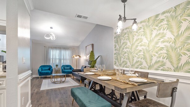Un comedor con una mesa de madera dispuesta para cuatro, sillas azules, un banco y una pared con un diseño de hojas.
