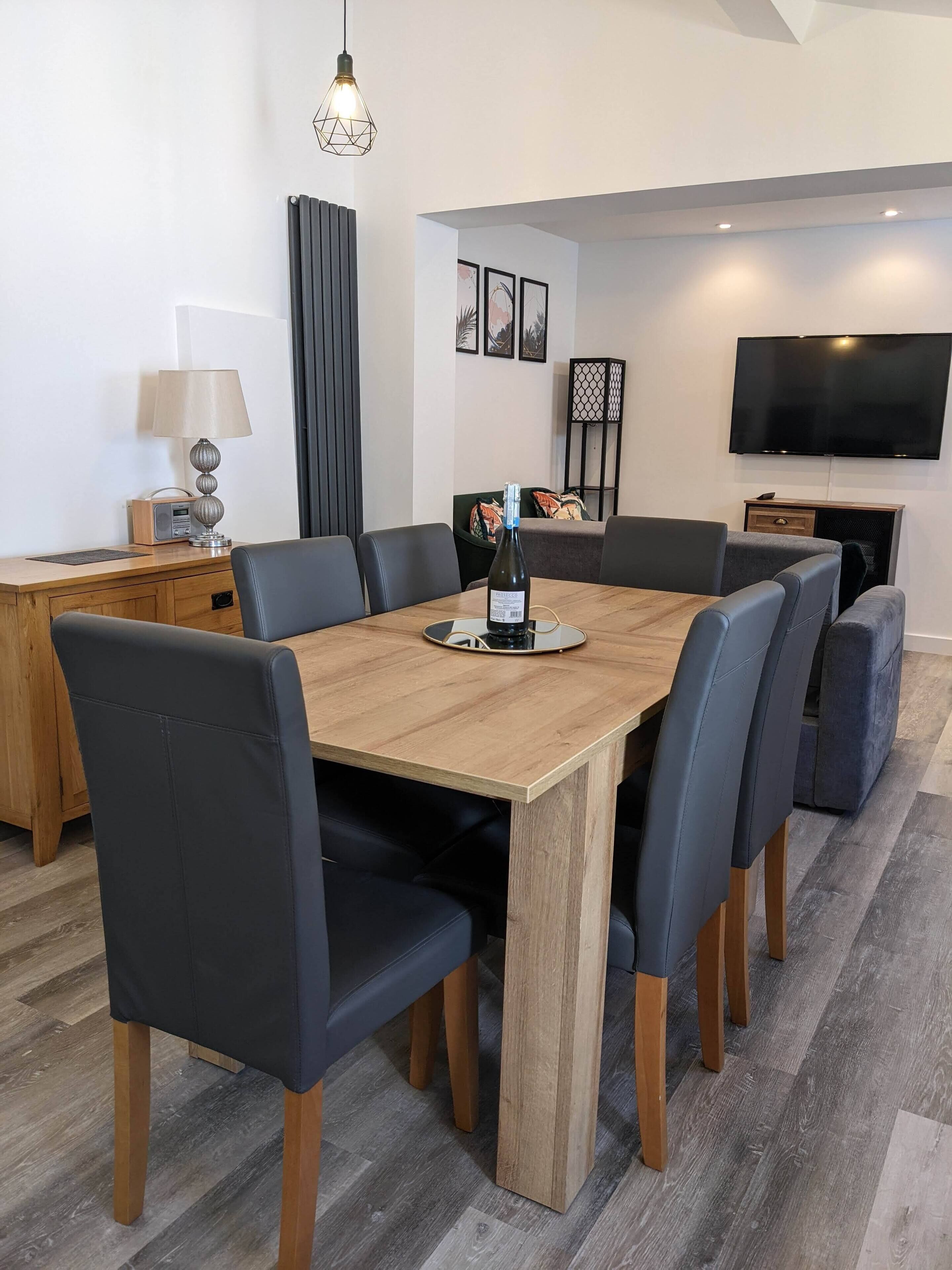 A modern dining area with a wooden table, black chairs, a lamp, a radio, and a bottle of wine.