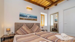Un dormitorio con una cama grande, una mesita de noche, un espejo y un cuadro de una playa.