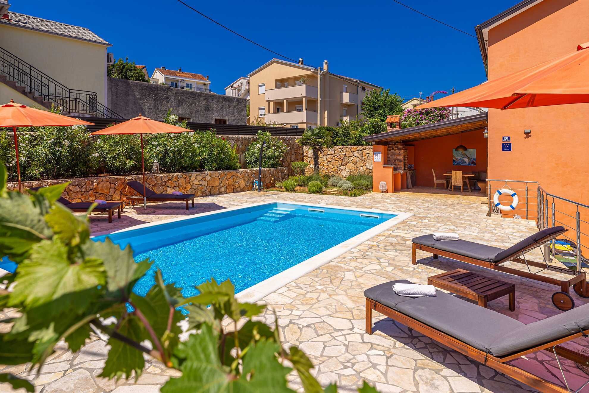 A swimming pool with lounge chairs and umbrellas, surrounded by stone walls and vegetation.