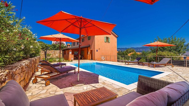 Zona de piscina con sillones de descanso, sombrillas y un muro de piedra.