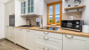 Una cocina moderna con armarios blancos, horno empotrado, cafetera, microondas y ventana con vistas.