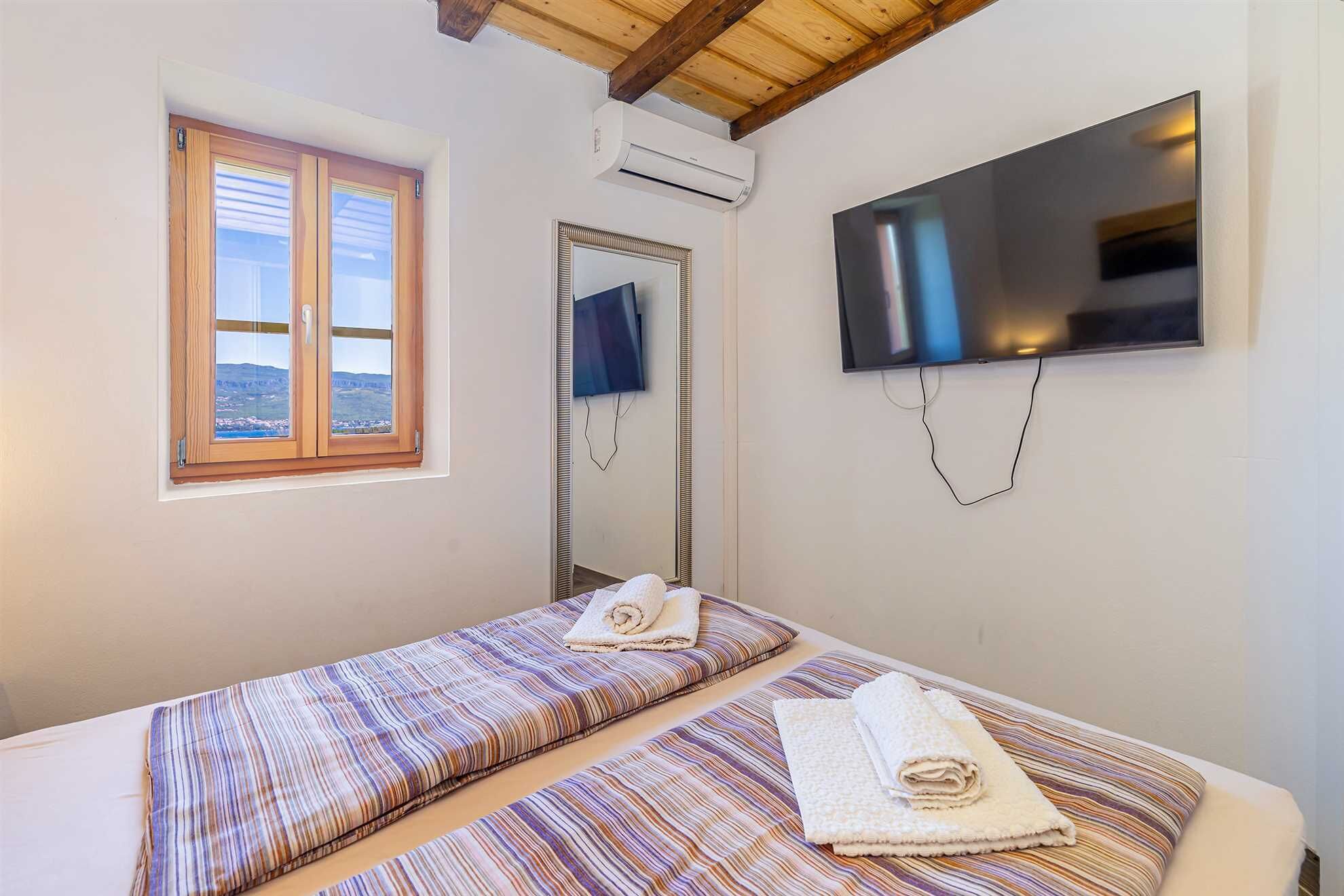 A room with two beds, a TV, an air conditioning unit, and a window with a view.