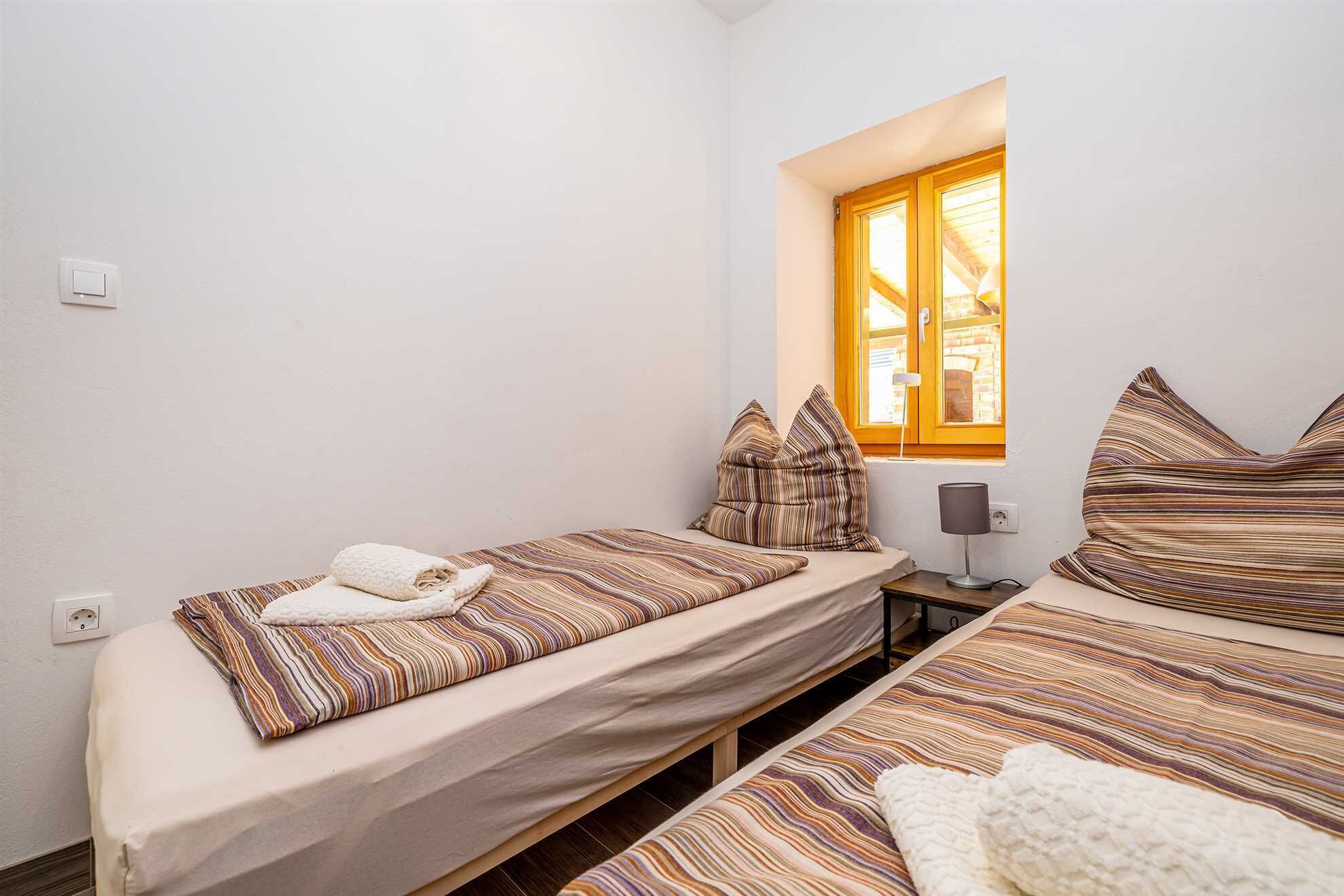 Een kleine, schone kamer met twee eenpersoonsbedden, een raam met uitzicht en een nachtkastje met lamp.