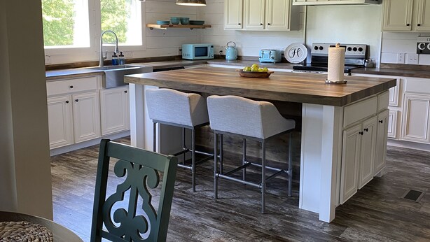 A kitchen with a central island, white cabinets, and a rustic ceiling.