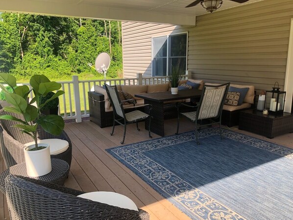 Una veranda coperta all'aperto con mobili in vimini, un tavolo da pranzo e un tappeto azzurro decorato.