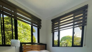 Une chambre à coucher avec un lit, une table de chevet, une lampe et deux fenêtres équipées de stores.