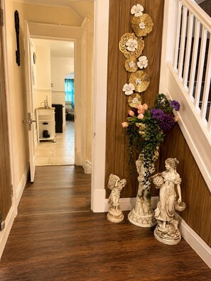 Een gang met een houten vloer, een witte leuning en een decoratieve wand met gouden bloemmotieven en een beeld van een figuur die manden draagt.