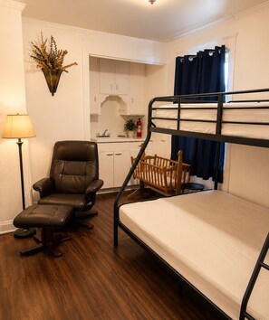 Un lit superposé avec une tête de lit en bois, un fauteuil en cuir, une petite table, une plante en pot et une lampe.